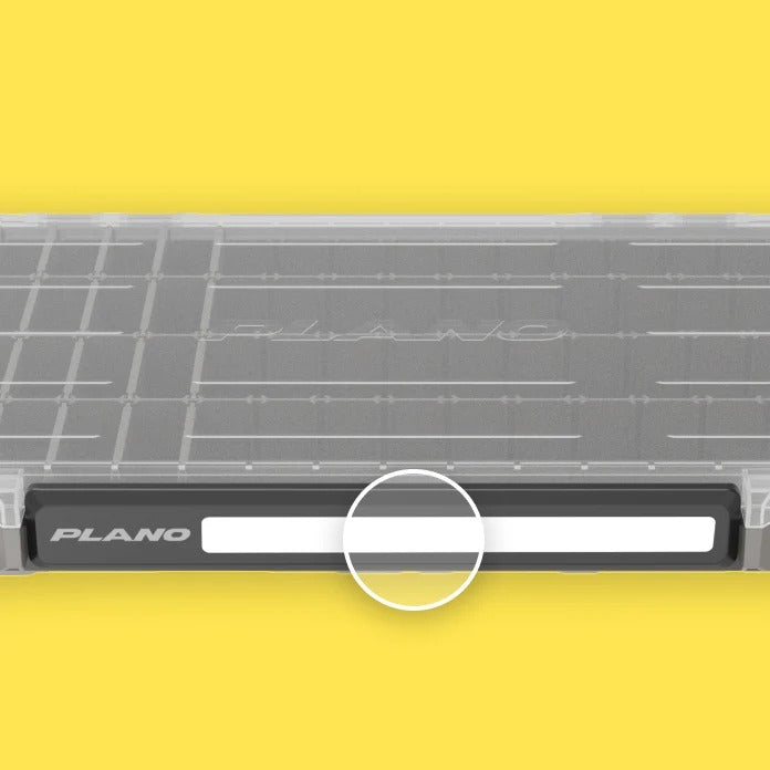 A close-up of a gray and black PLANO brand tackle organiser with a white bar on the front latch and a white circle overlay, to highlight the dedicated labelling area. The tackle box is set against a solid yellow background.