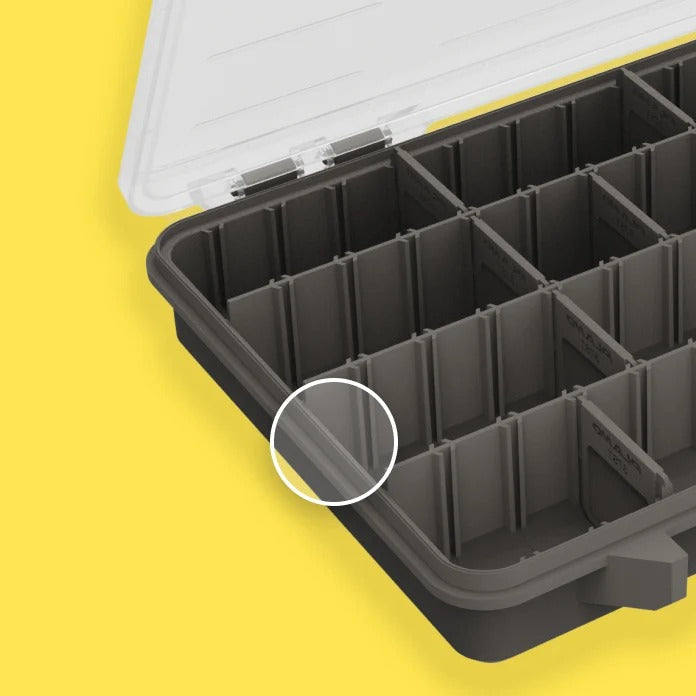 Close-up of a dark grey compartment organiser tray with a transparent lid, shown on a bright yellow background. A white circle highlights a small section of the grey tray to show Rustrictor technology.