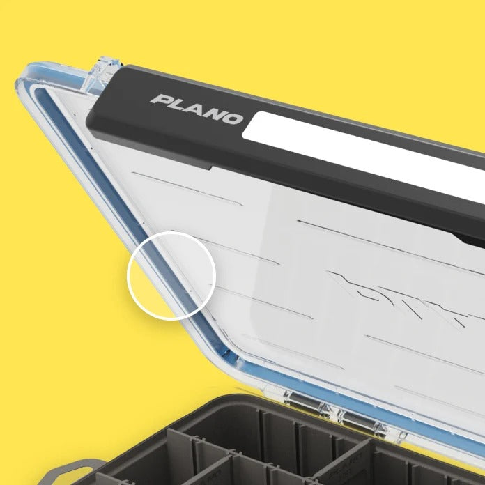 Close-up of a clear hard case with a black lid section labeled PLANO, shown open against a bright yellow background. The case has a white interior organizer panel and dark storage compartments.